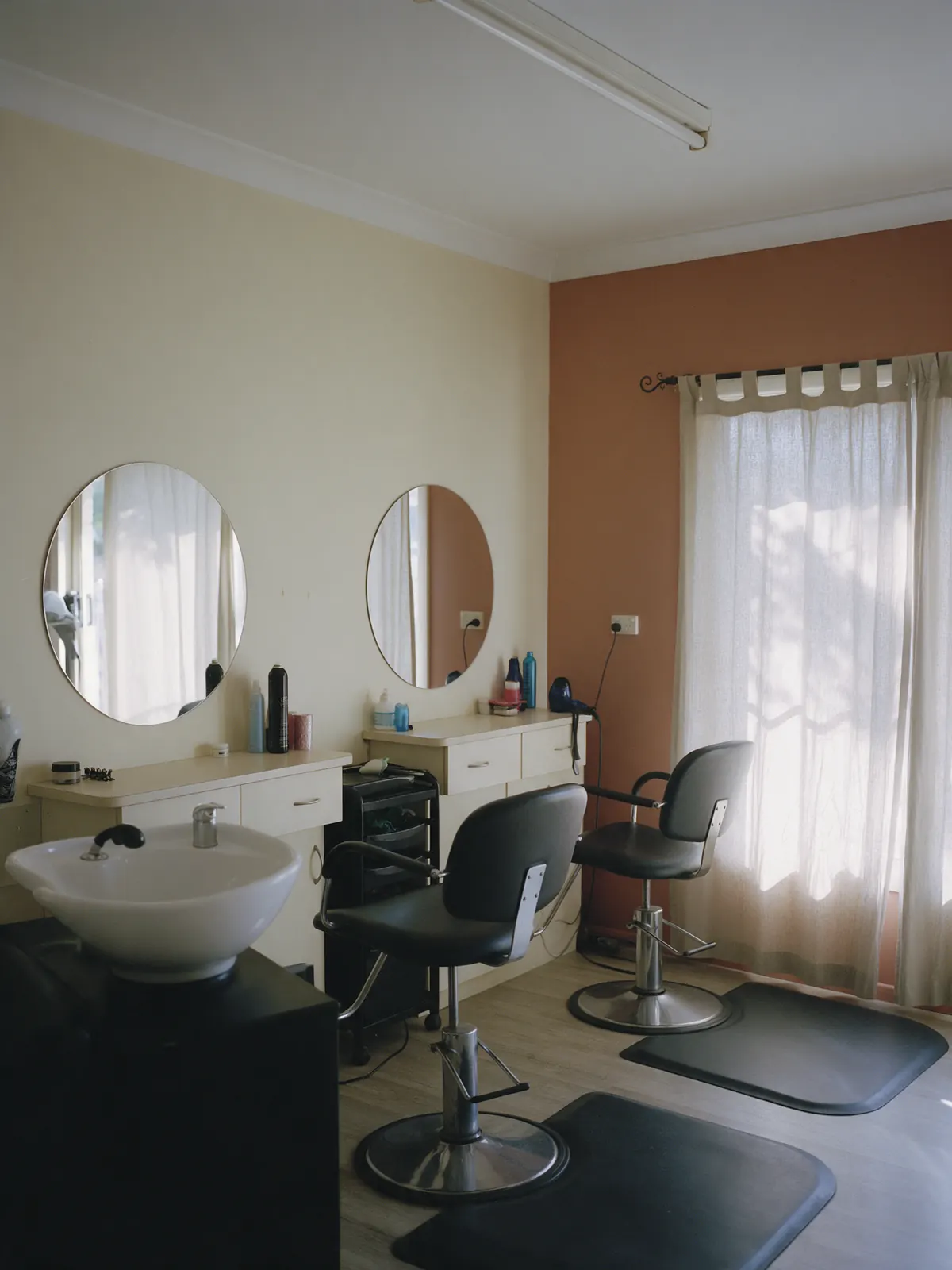 Inside the salon: two round mirrors, a basin and a terracotta wall